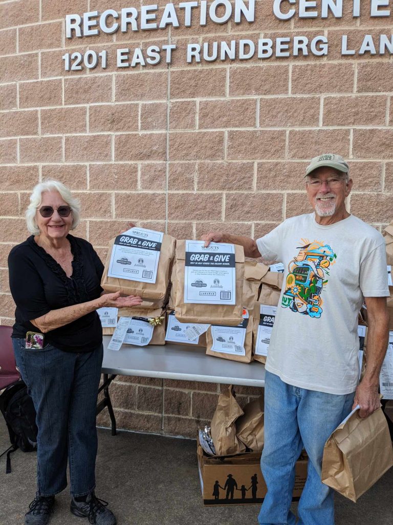 Carol and a volunteer hold up Sprouts donations